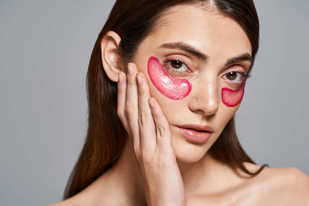 A young Caucasian woman with brunette hair wearing vibrant pink eye patches on her face, creating a bold and artistic look. - Fotoğraf, Görsel