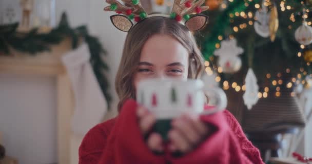 Retrato de una hermosa mujer joven sonriendo mientras sostiene la taza de café fresco durante la Navidad en casa - Metraje, vídeo
