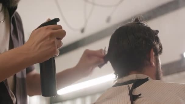 Recortado bajo ángulo de tiro de peluquería rociar el cabello del cliente con agua y el uso de peine, mientras que da corte de pelo en la barbería - Imágenes, Vídeo
