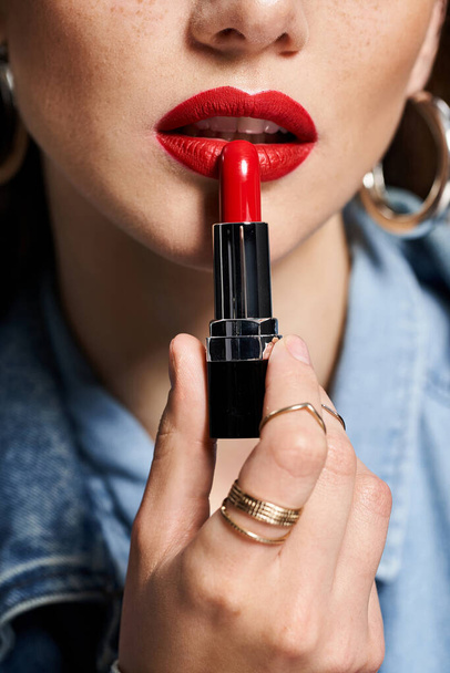 A young woman holds a vibrant red lipstick in her hand, poised to enhance her beauty. - Photo, Image