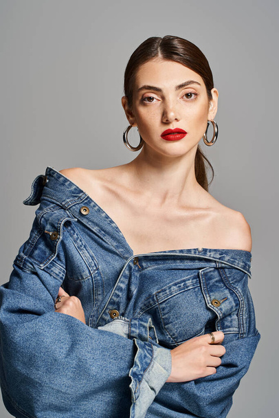 A young Caucasian woman with brunette hair wearing a trendy jean jacket and bold red lipstick. - Photo, Image