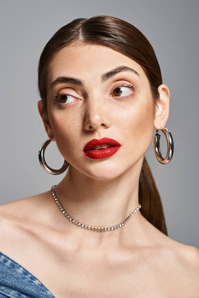 Una mujer caucásica joven con estilo en un estudio, con lápiz labial rojo y grandes pendientes de aro, exudando confianza y sofisticación. - Foto, imagen
