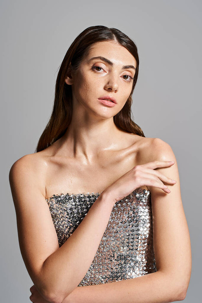 A young Caucasian woman with brunette hair poses in a stunning silver dress, exuding elegance and confidence. - Photo, Image