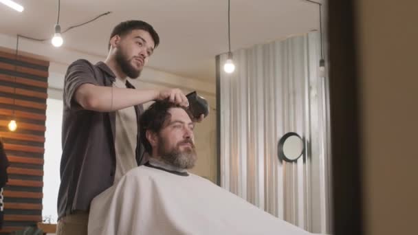 Professional parturi kuivaus hiukset mies asiakkaan isku kuivausrumpu jälkeen antaa hänelle hiustenleikkuun parturi - Materiaali, video