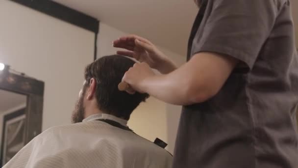 Low angle shot van professionele kapper borstelen haar van mannelijke klant na kapsel in salon - Video