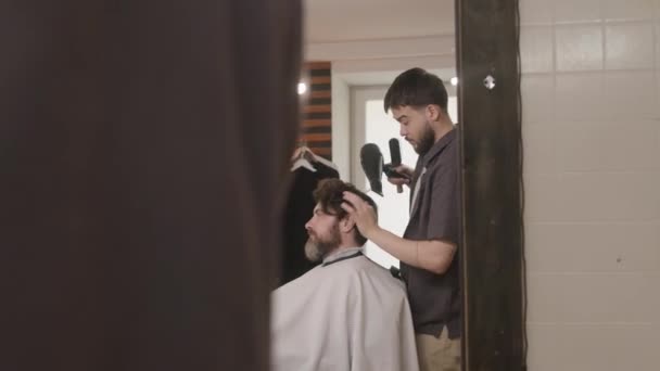 Reflejo espejo de peluquería secado pelo de cliente masculino con secador de pelo mientras le sirve en la barbería - Metraje, vídeo