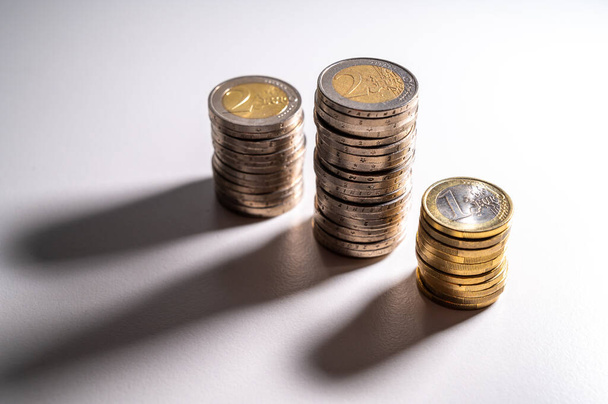Stapeln von Münzen nebeneinander, auf weißer Oberfläche, und ihre Schatten. Geldmenge, Währung und Reichtum. - Foto, Bild