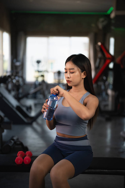 Glückliche asiatische Sportlerinnen trinken Wasser und ruhen sich nach dem Training im Fitnessstudio aus. Athletin Mädchen, die starke und gute Gesundheit und Kraft trainiert. Sportgesundheitliches Konzept. - Foto, Bild