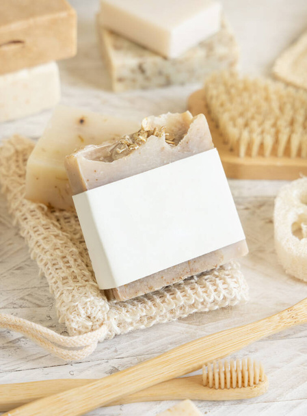 Barra de sabão bege artesanal orgânica com etiqueta em branco no saco de sabão perto de itens de higiene esponjas naturais e escova, escovas de dentes de bambu e cotonetes, close up, mockup - Foto, Imagem