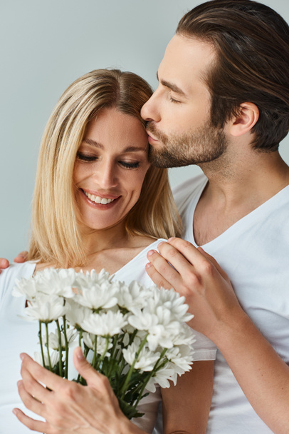 Un uomo bacia appassionatamente una donna mentre tiene in mano un mazzo di fiori, mostrando una fiorente connessione romantica tra loro.. - Foto, immagini