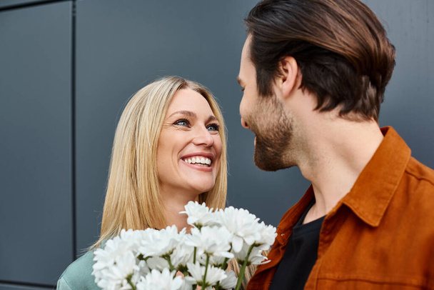 Mężczyzna stojący obok kobiety, podający jej bukiet białych kwiatów w romantycznym geście. - Zdjęcie, obraz