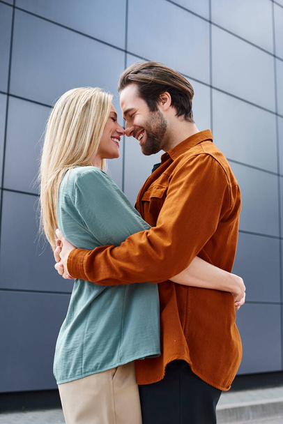 Um homem e uma mulher se envolvem em um abraço apaixonado na frente de um edifício elegante em um cenário da cidade. - Foto, Imagem