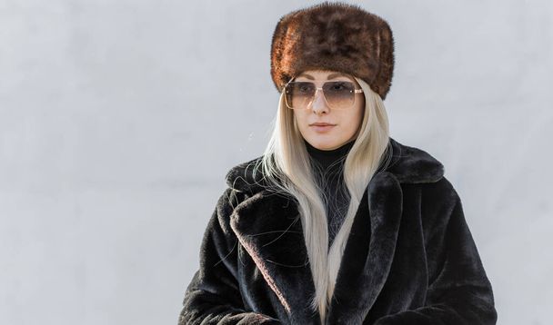 Slavic bimbo aesthetic. Portrait of a European type Blond head Young woman with natural skin in fur unisex hat.   - Photo, Image