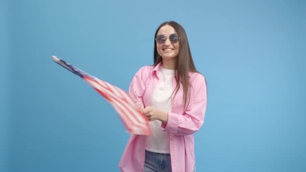 Amerikan gözlüklü, modaya uygun genç kız Amerikan bayrağı sallıyor, kutluyor, insan hakları ve özgürlüklerini kutluyor. Bağımsızlık Günü. Dişi dans ediyor. - Video, Çekim