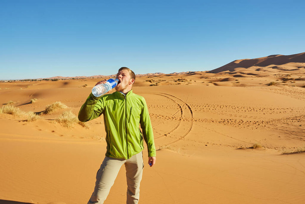 Un viajero solitario se encuentra entre las interminables dunas del Sahara, donde las arenas doradas se encuentran con el horizonte bajo el cálido sol. - Foto, Imagen