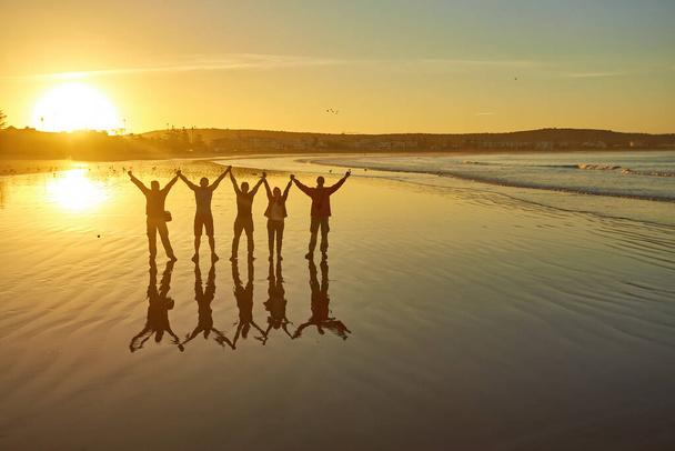 Siluety lidí pózujících proti ranní obloze vytvářejí podmanivou plážovou krajinu. Skupina turistů zachycuje klid úsvitu na pobřeží Atlantského oceánu v Essaouiře, Maroko. - Fotografie, Obrázek