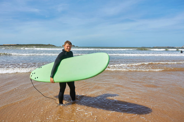 Ein junger Surfer posiert mit seinem Brett am Meer in Essaouira und fängt die Essenz der Surfkultur vor der malerischen Kulisse des Atlantiks ein - Foto, Bild
