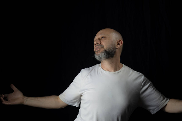 Bald, bearded man wearing casual clothes against black background. - Photo, Image