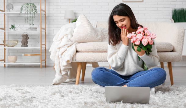 Jeune femme avec des roses et ordinateur portable assis sur le sol à la maison - Photo, image