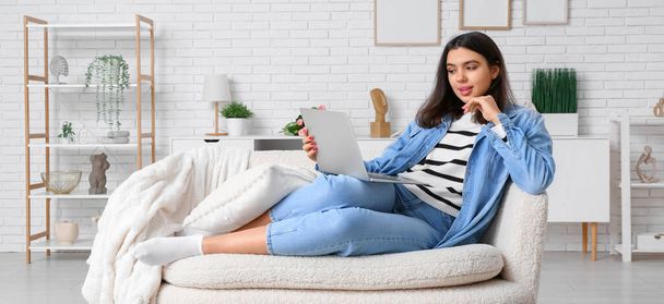 jeune femme avec ordinateur portable assis sur le canapé à la maison - Photo, image