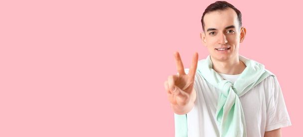 Young man showing victory gesture on pink background with space for text - Photo, image