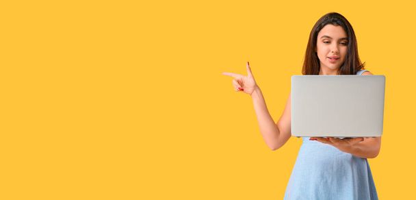 Junge Frau mit Laptop zeigt etwas auf gelbem Hintergrund mit Platz für Text - Foto, Bild