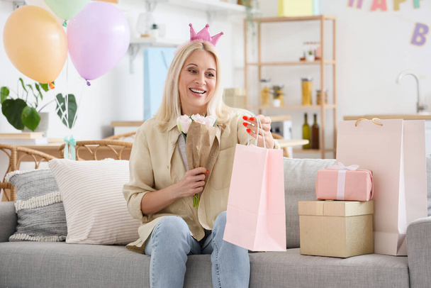 Bir buket çiçekli ve çantalı olgun bir kadın evde doğum gününü kutluyor. - Fotoğraf, Görsel