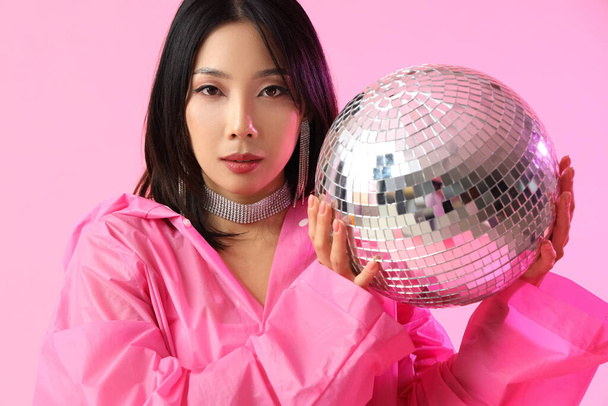 Moda joven mujer asiática en impermeable con bola disco sobre fondo rosa - Foto, Imagen