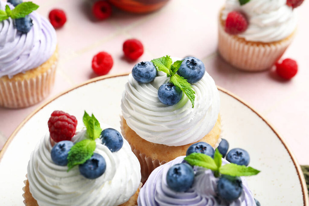 Prato de deliciosos cupcakes com mirtilos, framboesas e hortelã no fundo da telha rosa - Foto, Imagem