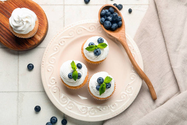 Plate of delicious cupcakes with blueberries and mint on white tile background - Photo, Image