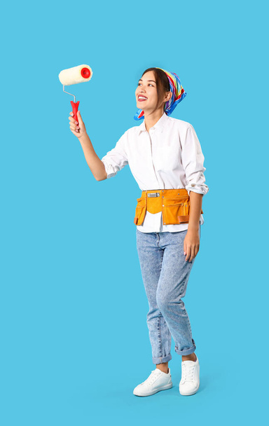 Женский азиатский декоратор с ролик краски на синем фоне - Фото, изображение