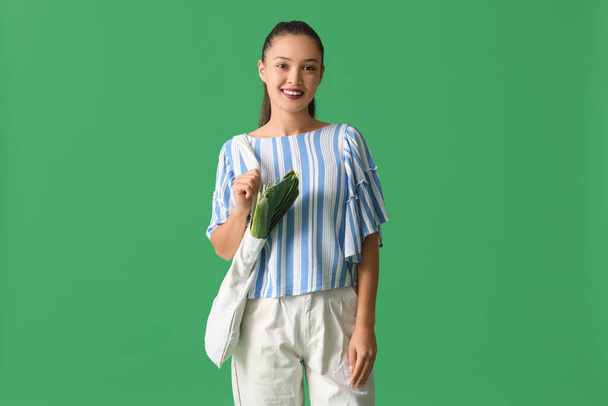 Jeune femme asiatique avec éco sac plein de nourriture fraîche sur fond vert - Photo, image