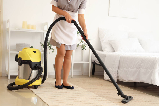 Kamermeisje schoonmaken hotelkamer met stofzuiger - Foto, afbeelding