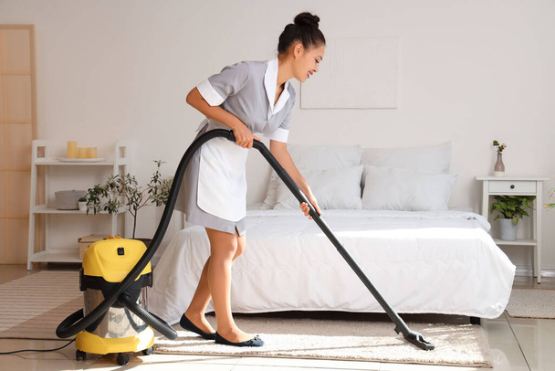 Hübsches Zimmermädchen reinigt Hotelzimmer mit Staubsauger - Foto, Bild