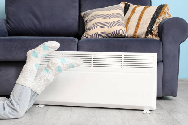 Woman in warm socks near electric heater at home. Concept of heating season - Photo, Image