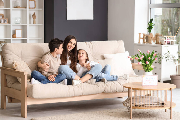 Молодая женщина с маленькими детьми, обнимающимися дома на диване. Праздник Дня матери - Фото, изображение