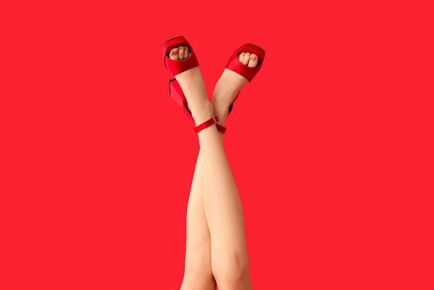 Jambes de belle jeune femme en talons hauts élégants sur fond rouge - Photo, image