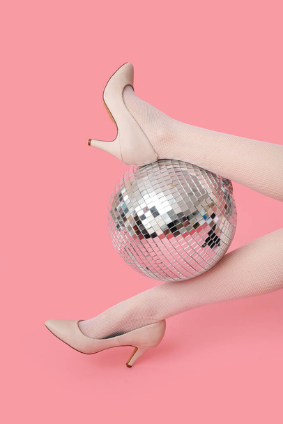 Γυναικεία πόδια σε μοντέρνα ψηλά τακούνια με ντίσκο μπάλα σε ροζ φόντο - Φωτογραφία, εικόνα