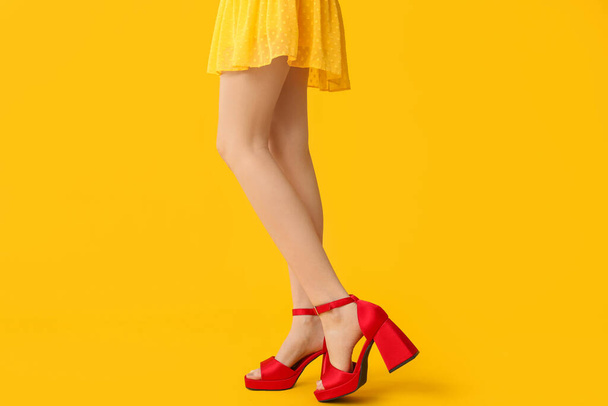 Ноги красивої молодої жінки в стильних високих підборах на жовтому фоні - Фото, зображення