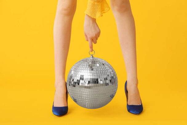 Женские ноги на модных высоких каблуках с диско шаром на желтом фоне - Фото, изображение