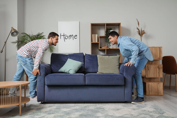 Handsome young brothers moving sofa in living room - Fotografie, Obrázek