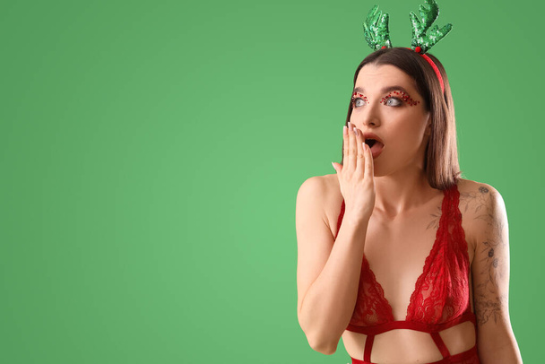 Beautiful young shocked woman in Christmas deer horns with stylish makeup on green background - Foto, Bild