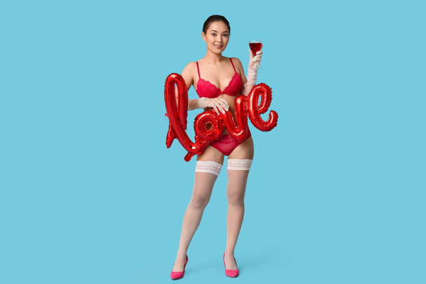 美しい若いセクシーなアジアの女性とワイングラスとブルーバックグラウンドで愛の言葉の形. バレンタインデーのお祝い - 写真・画像