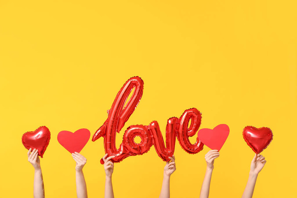 Manos femeninas con globos en forma de palabra AMOR y corazones sobre fondo amarillo. Celebración de San Valentín - Foto, imagen
