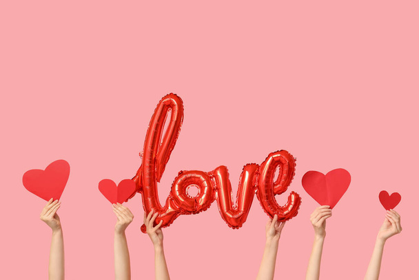 Female hands with balloon in shape of word LOVE and paper hearts on pink background. Valentine's Day celebration - Photo, Image