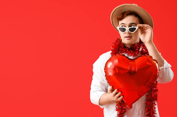 Jeune homme avec ballon en forme de coeur sur fond rouge. Fête de la Saint-Valentin - Photo, image