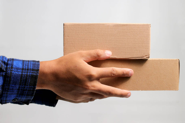 Een hand met een kartonnen doos tegen een grijze achtergrond, ter illustratie van het concept van de scheepvaart, levering en logistieke diensten - Foto, afbeelding