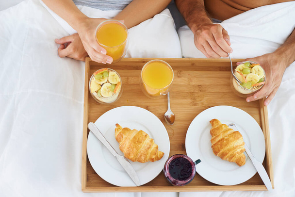 Couple, food and breakfast in bed for morning, wakeup or meat and snack together in relax at home. Top view of man and woman hands eating healthy for diet, nutrition or vitamin c juice in bedroom. - Photo, Image
