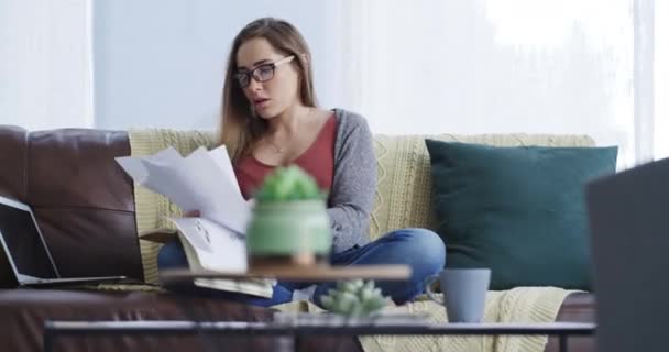 Stress, remote work and woman with documents on a sofa for difficult project with frustration. Upset, pressure and young female freelancer from Canada throw paperwork in living room at apartment - Footage, Video