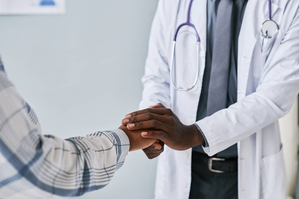 Close up of caring black doctor holding hands with female patient to support and comfort - Photo, Image